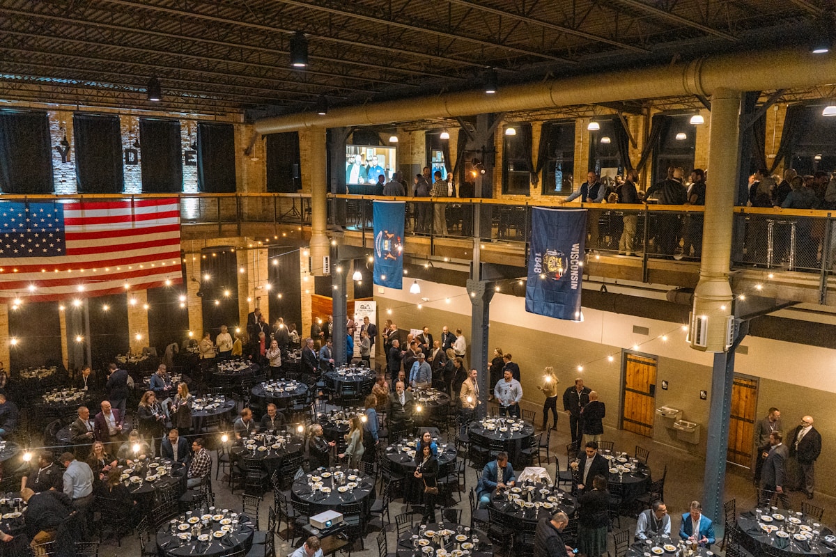 Warm brick-and-timber hotel banquet hall filled with convention attendees at round tables during an evening reception