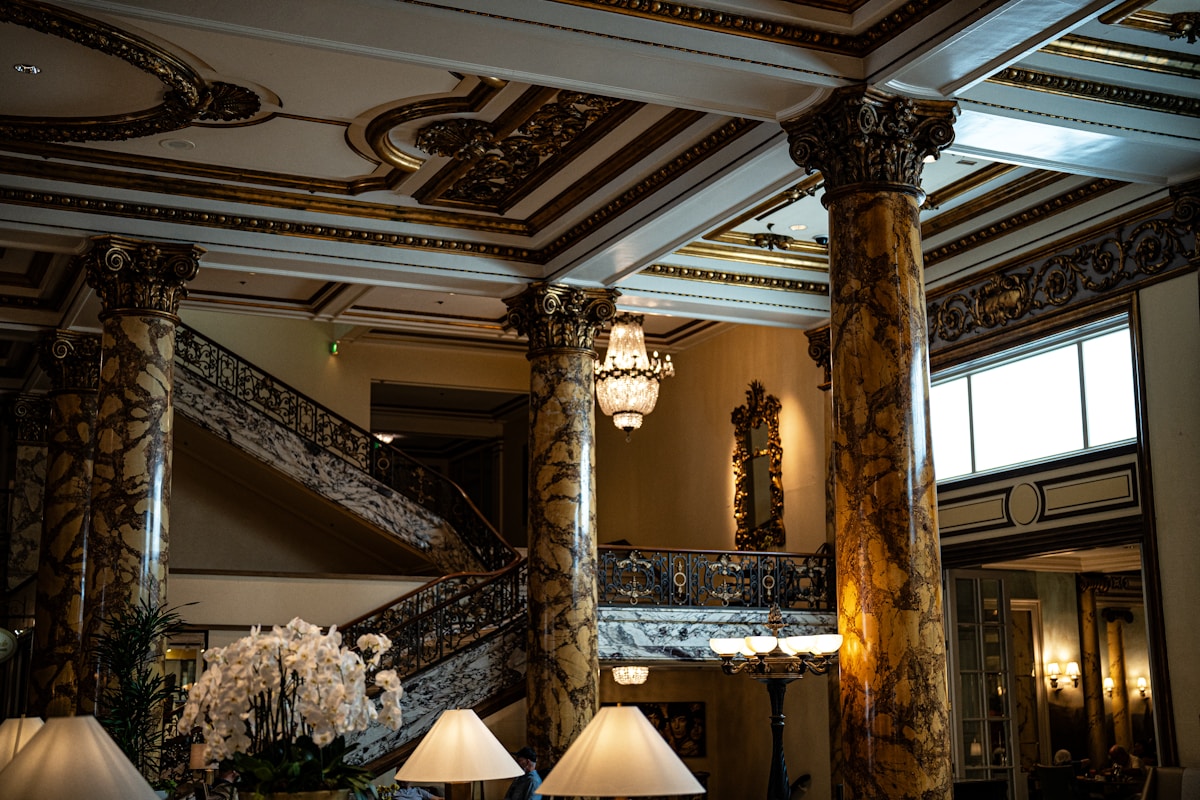 Grand historic hotel lobby with marble columns, ornate gilded plasterwork, a sweeping staircase and crystal chandeliers