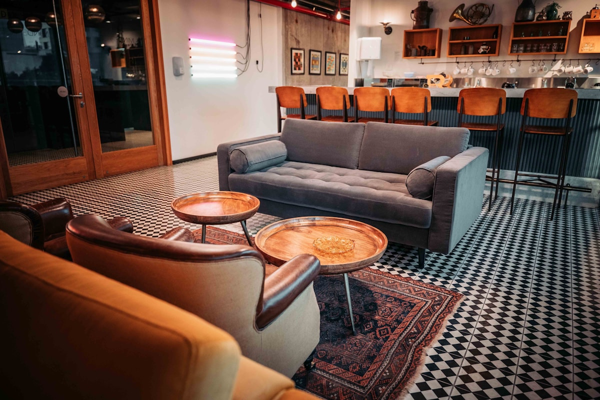 Warm hostel common room with lounge seating, a bar counter and stools, and patterned tile flooring